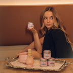 Woman holding a jar of cream with skincare products on a tray in front of her.
