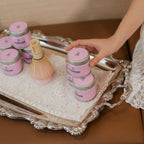 Person arranging pink jars on a decorative tray with a blurred background