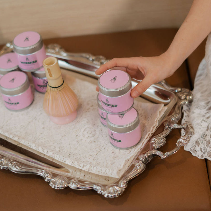 Person arranging pink jars on a decorative tray with a blurred background